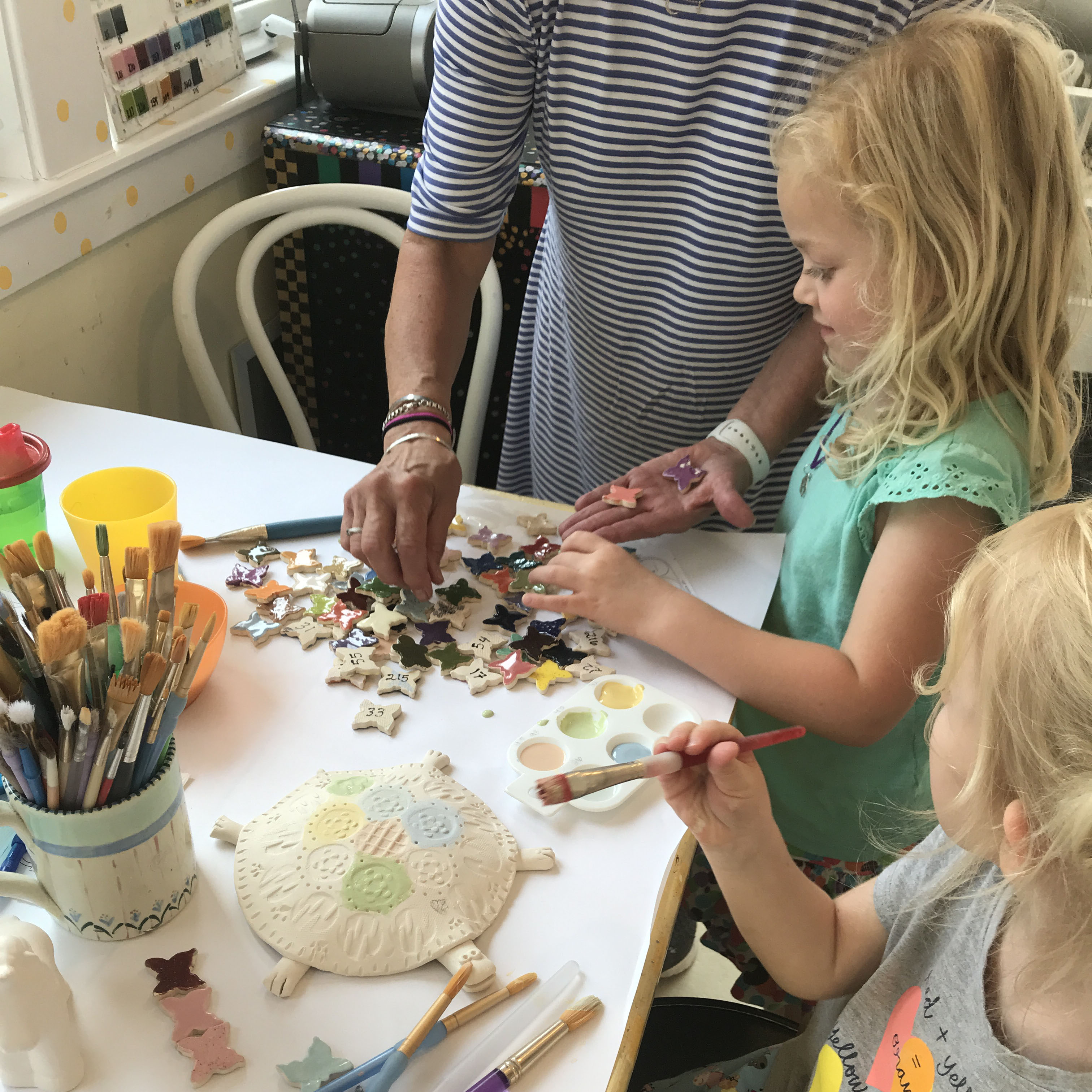 Children painting bisque pottery with an adult looking on